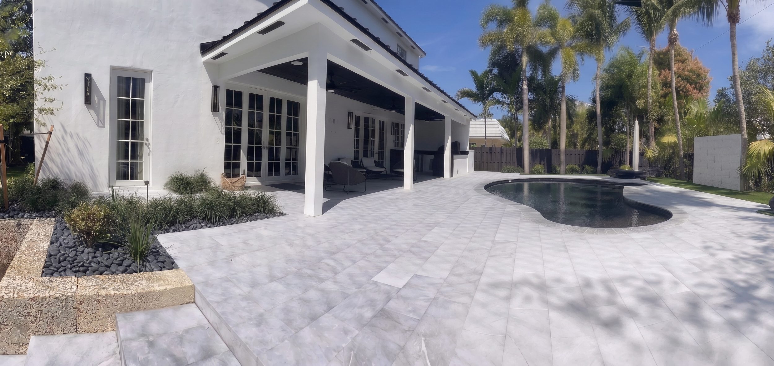Pool deck with natural-stone pavers, coral-stone planter walls, palms and artificial turf at a South Florida residence